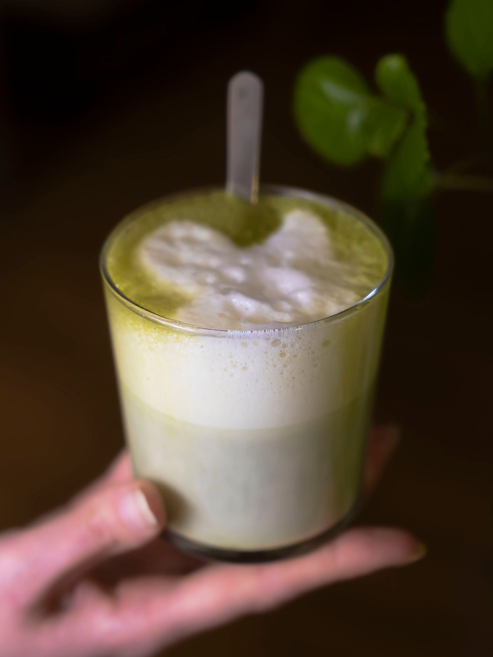 Hand hält ein Glas mit schaumigem grünem Matcha Latte